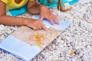 aanbiddelijk weinig meisje met kaart vind de manier Aan tropisch strand vakantie foto