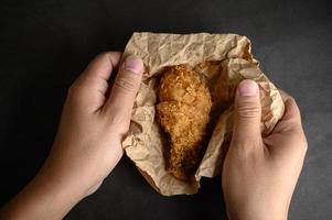 handen oppakken van krokant gebakken kip op bruin papier foto