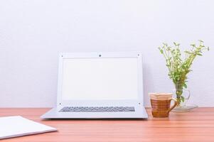 laptop, beker en bloem op het bureau foto