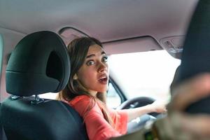 vrouw in auto, draaien in de omgeving van op zoek Bij passagiers in terug stoel idee taxi bestuurder. concept van tentamen voertuig. terug visie van een aantrekkelijk jong zakenvrouw op zoek over- haar schouder terwijl het rijden een auto. foto