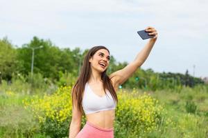 jong sportief vrouw nemen een selfie Bij park. ze is op zoek Bij camera. een aantrekkelijk vrouw loper nemen selfie buiten. foto