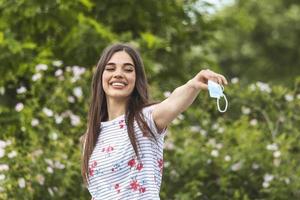 vrouw het werpen weg haar masker. jong gelukkig meisje op zoek Bij beschermend medisch masker, nemen uit verwijderen masker van haar gezicht. einde van pandemisch coronavirus concept. ncov, covid 19. stuifmeel allergie Bij voorjaar foto