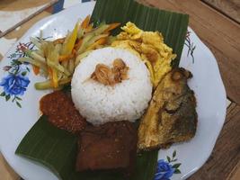 een deel van nasi kucing compleet met gebakken melkvis hoofd, tofu, geserveerd Aan een bord met banaan bladeren. foto