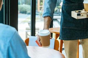 Aziatisch personeel vervelend schort portie heet zwart koffie kop naar klant Aan tafel in cafe koffie winkel, cafe restaurant, klein bedrijf baasje, onderhoud verstand, nieuw normaal, voedsel en drinken levering concept foto