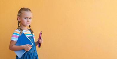 slim schoolmeisje kind in bril in school- uniform houdt gekleurde potloden, notitieboekje, leeg kopiëren ruimte geïsoleerd Aan geel achtergrond terug naar school- foto