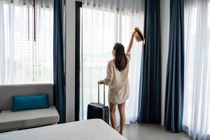 jonge vrouw reiziger met bagage kijken naar uitzicht in hotelkamer op zomervakantie foto