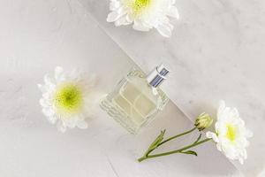 een fles van vrouwen parfum met een bloemen geur is bekleed Aan marmeren tegels met wit bloemen. modieus concept van natuurlijk materialen en aroma. foto
