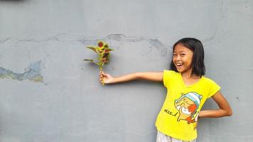 weinig meisje Holding jong fabriek. groen bladeren. ecologie concept. licht kleur achtergrond. foto