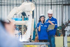 ingenieurs team monteur gebruik makend van computer controleur robot arm voor lassen staal in staal fabriek werkplaats. industrie robot programmering software voor geautomatiseerd fabricage technologie foto