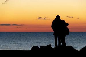 geliefden knuffelen in voorkant van de zee Bij zonsondergang foto