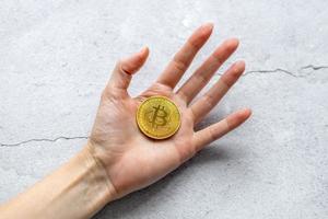 de concept van virtueel cryptogeld. bitcoin geld. een hand- Holding een gouden munt, Aan een grijs achtergrond. foto