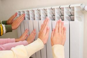 de familie verwarmt hun handen in de buurt de radiator. foto