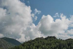 mooi visie van de bergen met pijnboom bomen en wit pluizig wolken, panoramisch schot van de bergen Bij middag Aan de Egeïsch kust foto