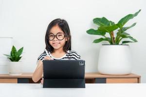 Aziatisch kind meisje leerling Wauw opgewonden Aan video telefoontje aan het leren naar aan het studeren online klasse of persoon leren van huis school- met tablet foto