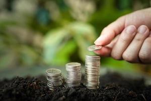 vrouw hand- is zetten zilver munten Aan stapel zilver munten met groen natuur achtergrond. geld besparing en bedrijf financiën concept, bedrijf groei en geld toekomst, financieel succes foto