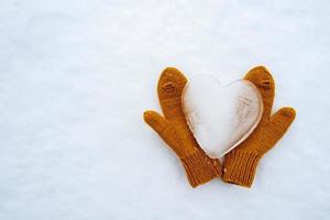 hart symbool van liefde, gemaakt van ijs, Aan warm geel gebreid wanten, Aan de sneeuw. Valentijnsdag dag. kopiëren ruimte. conceptueel. top visie. foto