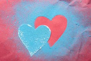 Valentijnsdag dag. twee harten zijn een symbool van liefde, een besprenkeld met helder blauw poeder en de andere Aan een rood getextureerde achtergrond. foto