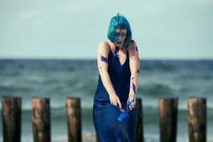 artistieke blauwharige vrouw performancekunstenaar in jurk besmeurd met blauwe gouacheverf op haar lichaam foto