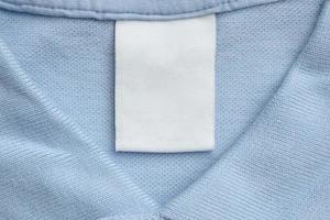 wit blanco wasserij zorg kleren etiket Aan blauw overhemd kleding stof achtergrond foto