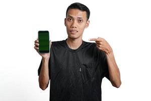 opgewonden Aziatisch Mens vervelend zwart training t-shirt, richten Bij groen scherm van smartphone. geïsoleerd door wit achtergrond foto