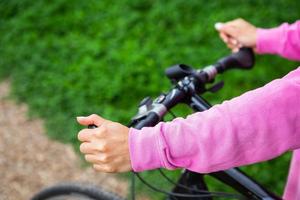 een meisje in een roze sweater houdt Aan naar de stuur van een fiets, een fiets rijden in de park. buitenshuis recreatie is mooi zo voor Gezondheid. foto
