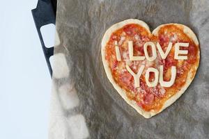 Italiaans hart vormig pizza met salami, tomaat saus, parmezaan, pizza saus, Mozzarella en olijf- olie Aan perkament papier met kaas ik liefde jij. liefde concept voor Valentijnsdag dag februari 14. foto