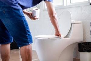 Mens Holding zakdoek papier en veeg schoongemaakt de doorspoelen toilet van de openbaar toilet voordat gebruik makend van het voor bescherming tegen bacterieën, de concept van hygiëne in dagelijks leven. foto