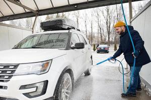 Mens het wassen Amerikaans suv auto met dak rek Bij een zelf onderhoud wassen in verkoudheid het weer. foto