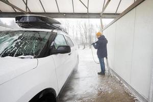 Mens het wassen hoog druk water Amerikaans suv auto met dak rek Bij zelf onderhoud wassen in verkoudheid het weer. foto