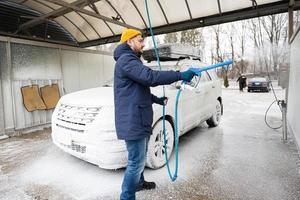 Mens het wassen Amerikaans suv auto met dak rek Bij een zelf onderhoud wassen in verkoudheid het weer. foto