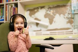 jong meisje vervelend koptelefoon, geniet haar afgelegen onderwijs. ver weg aan het studeren, thuisonderwijs. tonen duim omhoog. foto