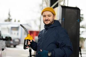 Mens houden brandstof pomp terwijl tanken zijn auto Bij de gas- station in verkoudheid het weer. foto