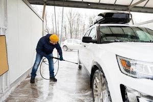 Mens het wassen hoog druk water Amerikaans suv auto met dak rek Bij zelf onderhoud wassen in verkoudheid het weer. foto