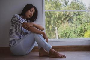 een Aziatisch vrouw gevoel verdrietig en eenzaam zittend door de venster in de huis. verwardheid, teleurstelling, en mentaal problemen foto