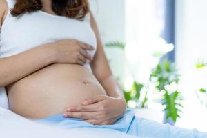 zwanger Dames licht houden maag met handen. een zwanger vrouw is gelukkig naar praten naar baby. moeder en zoon's liefde concept foto