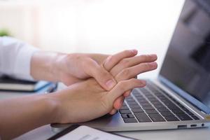 bedrijf vrouw drukken de midden- van haar palm met haar duim naar verlichten pijn ten gevolge naar een tendinitis veroorzaakt door een buitensporig gebruik van computer. foto