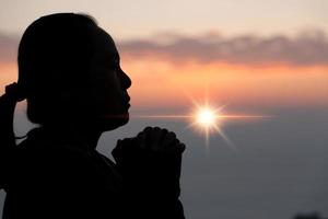 geloof van christen concept. geestelijk gebed handen over- zon schijnen met wazig mooi zonsondergang achtergrond. vrouw handen aanbidden god met liefde en vertrouwen. silhouet van een vrouw bidden met een kruis. foto