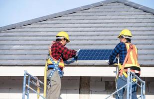 een team van Aziatisch technici installeert zonne- panelen Aan de dak van een huis. dwarsdoorsnede visie van bouwer in helm installeren zonne- paneel systeem concept van hernieuwbaar energie foto