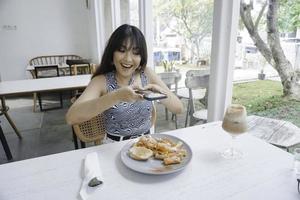 glimlachen gewoontjes vrouw nemen een afbeelding van pasta Aan een wit bord met mobiel telefoon terwijl zittend Bij de restaurant foto