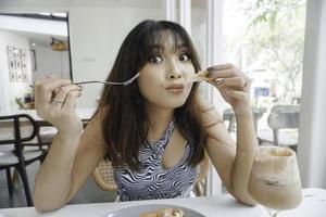grappig jong Aziatisch vrouw aan het eten smakelijk pasta in cafe foto