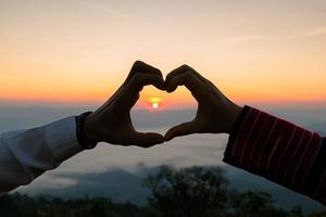 silhouet van bruiloft paar in liefde hand- teken hart gedurende zonsopkomst met ochtend- lucht achtergrond. pre-huwelijk portretten gelukkig paar afbeeldingen Mens en vrouw met lucht natuur achtergrond. foto