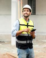 mannetje architect of ingenieur gebruik makend van mobiel telefoon voor communicatie terwijl werken Bij bouw plaats. professioneel gebouw aannemer staand Bij behuizing ontwikkeling plaats toepassingen smartphone Aan de functie. foto