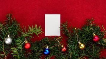 stuk van papier voor Kerstmis wensen Aan een rood achtergrond met takken van Kerstmis boom en Kerstmis ballen. foto