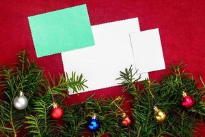 stuk van papier voor Kerstmis wensen Aan een rood achtergrond met takken van Kerstmis boom en Kerstmis ballen. foto
