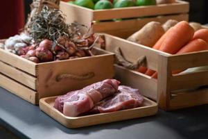 rauw varkensvlees is gelegd in voorkant van groente, aardappel, wortel, sjalot, limoen, ui, tomaat dat in hout doos. met studio licht omgeving. foto