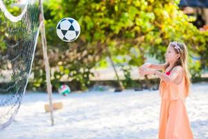 weinig actief meisje spelen volleybal Aan strand met bal. sportief flikker genieten van strand spel buitenshuis foto