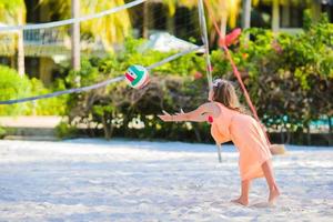 weinig actief meisje spelen volleybal Aan strand met bal. sportief flikker genieten van strand spel buitenshuis foto