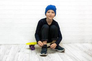 jongen in een hoed ritsen omhoog zijn sportschoenen terwijl zittend Aan een skateboard in neon licht foto