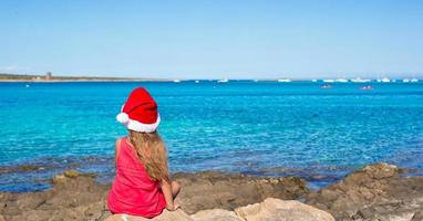 terug visie van schattig weinig meisje in de kerstman hoed Aan de strand foto