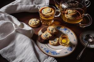 fotografie van een bord van koekjes en een glas van thee Aan een tafel met een kleding en een servet Aan het foto